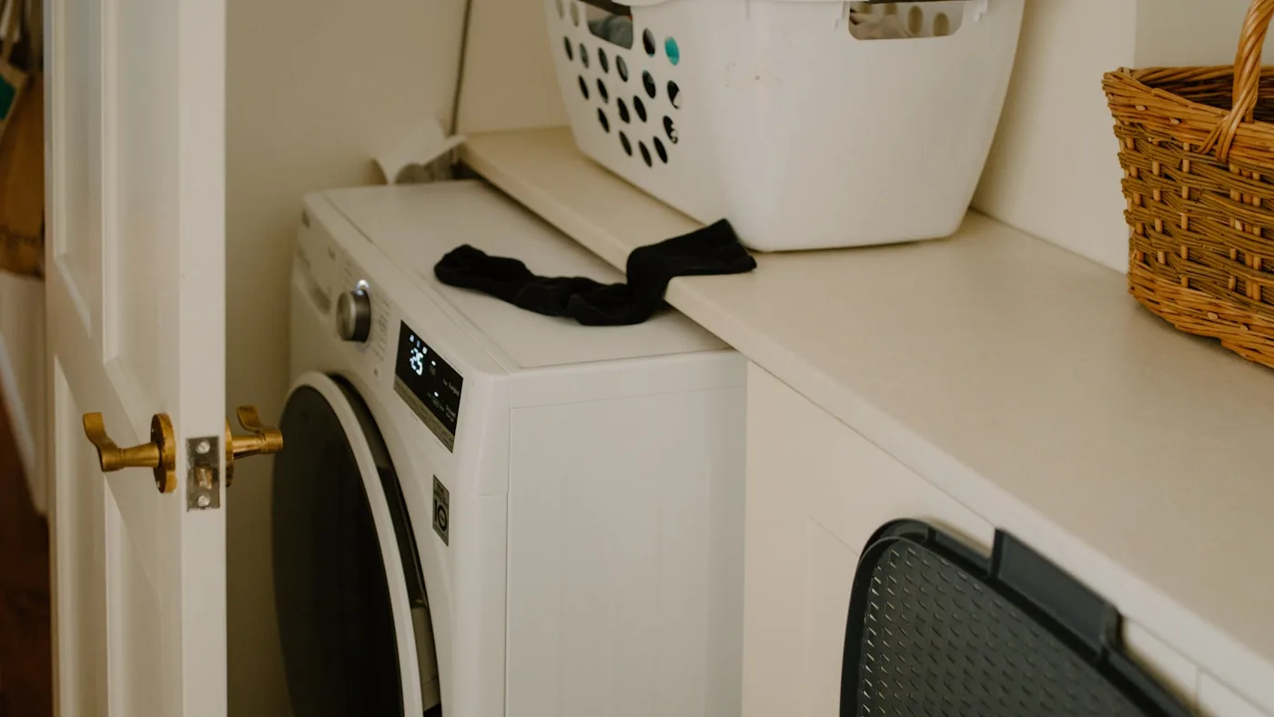 Un lave-linge hublot blanc encastré dans une buanderie, avec un panier à linge posé au-dessus