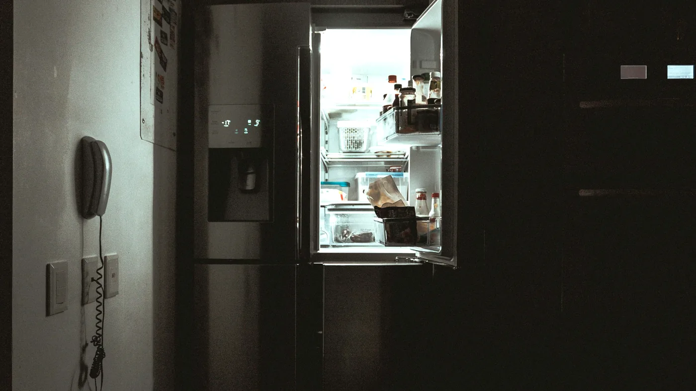 Un réfrigérateur porte ouverte dans une cuisine sombre, éclairé de l'intérieur